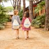 Due bambine camminano tenendosi la mano, con zainetti bianchi su un sentiero tra alberi.