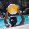 Una bambina in piscina tiene in alto una palla gonfiabile gialla e bianca.