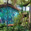 Una parete colorata con un murale astratto circondata da alberi e piante.