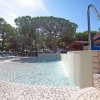 Una piscina con acqua cristallina, doccia a cascata e lettini, circondata da alberi.