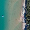 Spiaggia dall'alto con mare turchese e ombrelloni bianchi.
