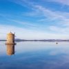 Un mulino a vento riflesso in un lago calmo sotto un cielo azzurro.