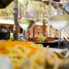 Due bicchieri di vino bianco su un tavolo con piatti di pasta e antipasti sullo sfondo.