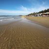 Una spiaggia sabbiosa con onde, ombrelloni e colline coperte di vegetazione sullo sfondo.