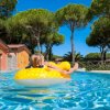 Bambina su ciambella gialla in piscina, circondata da alberi.