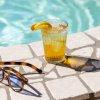 Bicchiere di tè freddo con arancia e occhiali da sole sul bordo piscina.