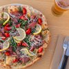 Pizza con bresaola, rucola e limone su tavolo con birra e posate.