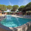 Piscina all'aperto con sedie a sdraio, circondata da alberi e case basse sotto un cielo azzurro.