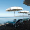 Ombrelloni bianchi e lettini su una spiaggia sabbiosa con vista mare.