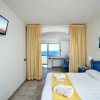Camera bianca con letto e tende gialle, vista mare.