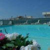 Piscina con lettini bianchi su un terrazzo, fiori in primo piano.