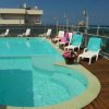 Piscina con solarium, lettini bianchi e asciugamani colorati su una terrazza.