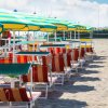 Spiaggia con ombrelloni a righe gialle verdi e lettini colorati in fila.