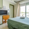 Camera con letto verde, TV su mobile, finestra con tende e balcone.