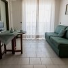 Mini appartamento con divano verde, tavolo con tenda, microonde e grande finestra con tenda bianca.