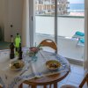 Tavolo rotondo con piatti di pasta e bevande davanti a un balcone con vista mare.