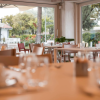 Ristorante con ampie finestre, tavoli apparecchiati e vista sul giardino.