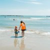 Una donna e un bambino camminano verso il mare, entrambi con secchielli colorati in mano.