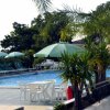 Piscina con ombrelloni verdi e tavolini bianchi.
