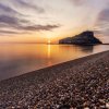 Tramonto su una spiaggia di ciottoli con l'isola in lontananza.