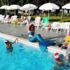 Una persona vestita da sirena accanto a bambini in piscina.