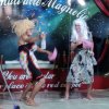 Persone sul palco indossano abiti colorati e divertenti parrucche.