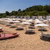 Spiaggia con lettini, ombrelloni bianchi e barca di salvataggio rossa.