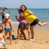 Persone che giocano e si divertono sulla spiaggia. Sullo sfondo, il mare e una torre.