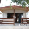 Bungalow con veranda in legno, circondato da alberi.